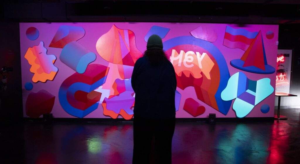 A guest observes the exhibit "Glorious Vision of a Rainbow," a wall of cut and painted wood.