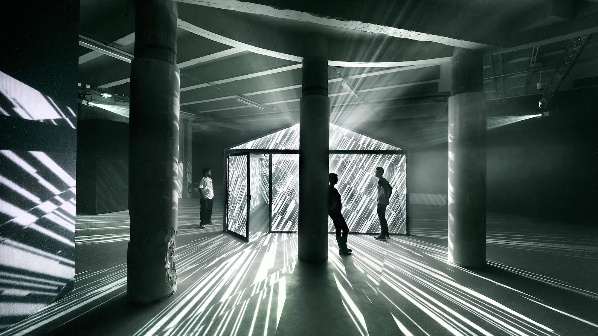 A glass shed emanating white light with guests milling around the outside observing the light show.